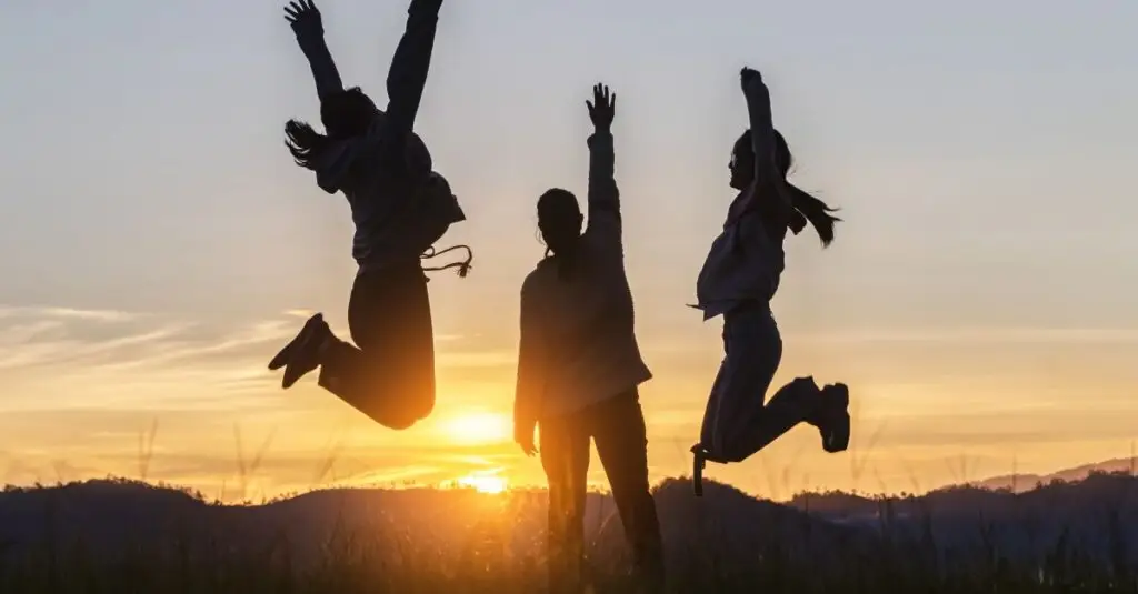 Three people jumping and celebrating together at sunset, representing the energy, connection, and trust that help teams collaborate effectively.