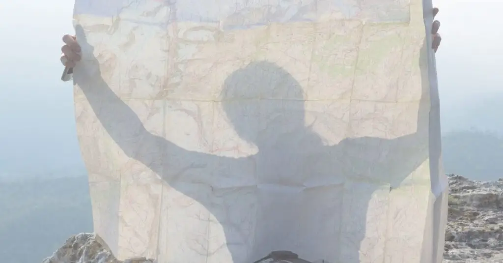 A person holding a large paper map while standing on a mountaintop, symbolizing leadership decision-making in uncertain and changing conditions.