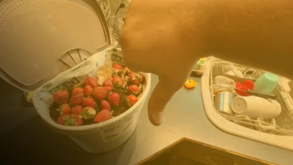 A hand giving a thumbs-down over a container of spoiled strawberries beside a kitchen sink, illustrating food waste, rising grocery costs, and the importance of reducing household waste.