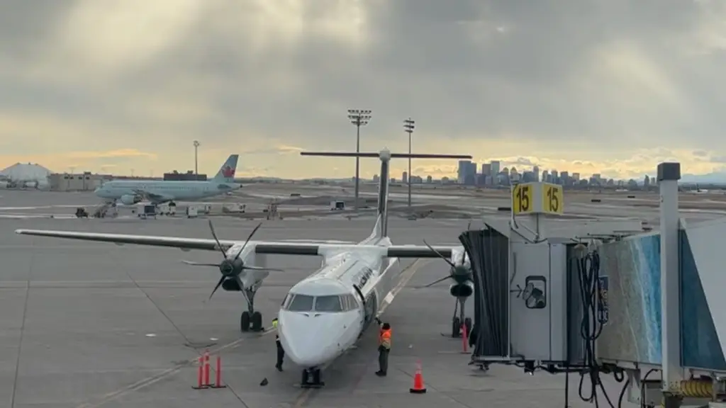 A regional aircraft parked at an airport gate with the Calgary skyline visible in the distance under a cloudy sky, symbolizing business travel and time spent on the road.