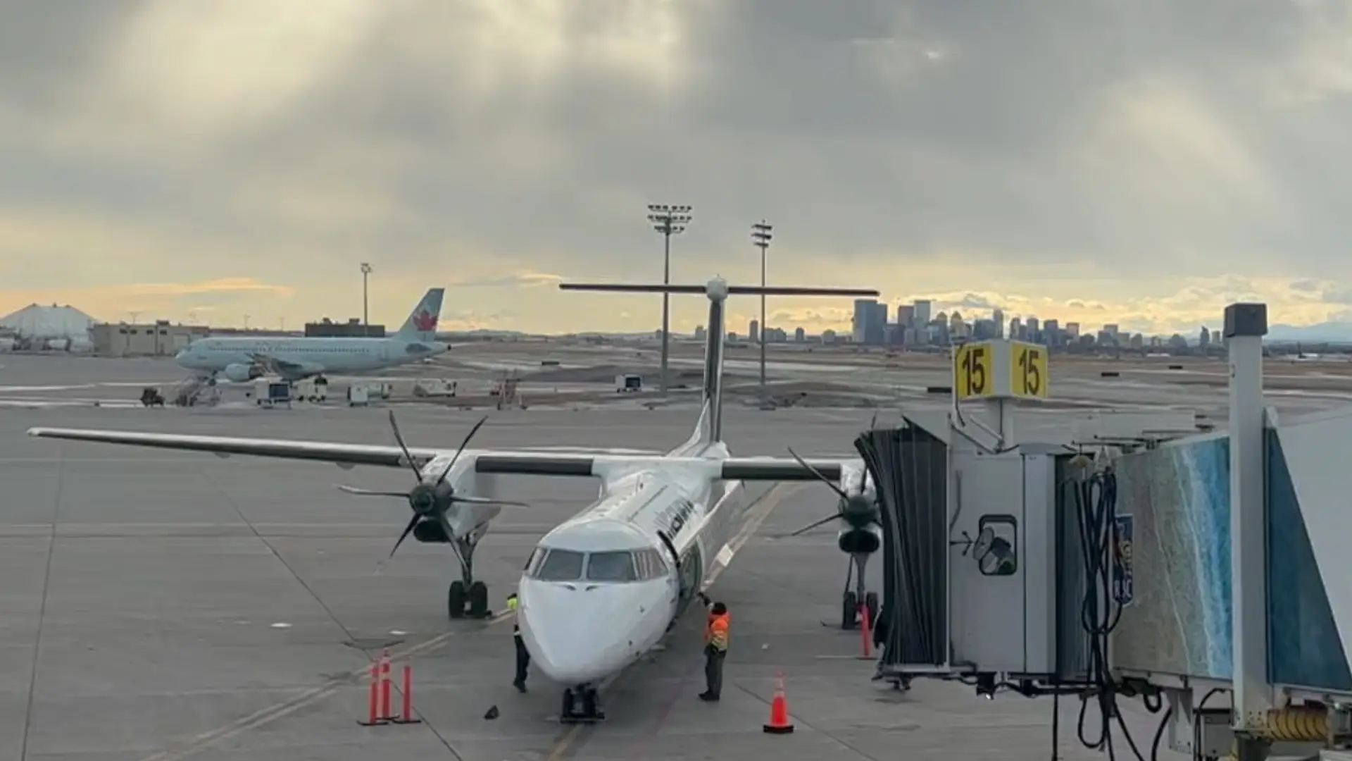 A regional aircraft parked at an airport gate with the Calgary skyline visible in the distance under a cloudy sky, symbolizing business travel and time spent on the road.